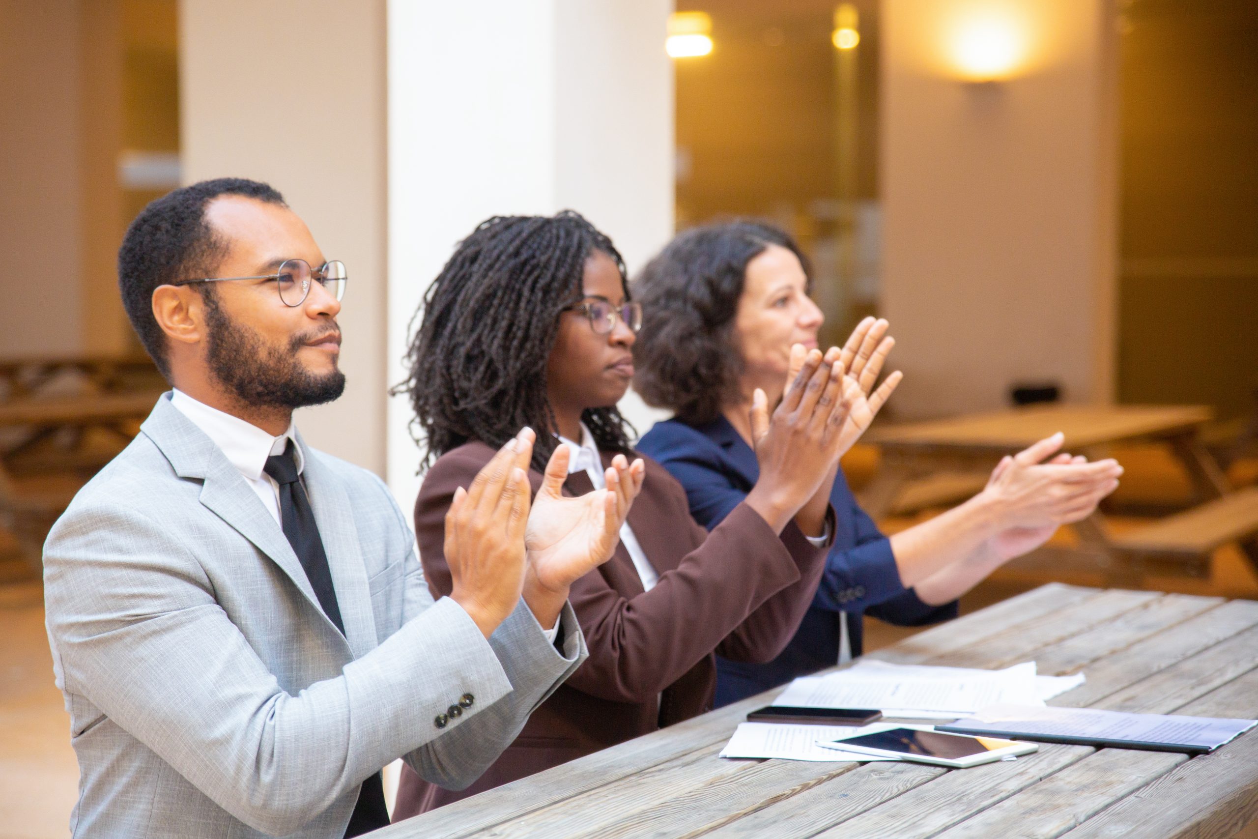 Excited inspired business people applauding speaker during conference. Business man and women sitting at table outside, looking into distance and clapping hands. Applause concept